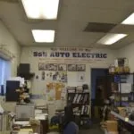 Interior of S&N Auto Electric shop with welcome sign, workbenches, shelving, and fluorescent ceiling lights