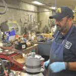 Mechanic in navy cap and apron working on engine component in cluttered workshop
