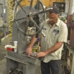 Mechanic in tan work shirt inspecting large wheel on industrial machine in workshop