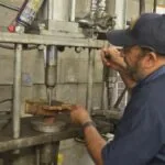Technician in navy cap and shirt operating industrial press equipment in workshop