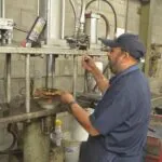 Technician in blue uniform and cap working on industrial electrical equipment mounted on concrete wall