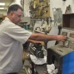 Technician in light blue shirt adjusts controls on electrical testing equipment in auto repair workshop
