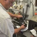 Technician working on electric motor component at workbench with tools and electrical equipment mounted on wall