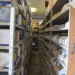 Narrow aisle between metal shelving units stocked with auto parts in a warehouse storage room
