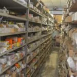 Industrial warehouse aisle with metal shelving units stocked with cardboard boxes and automotive parts