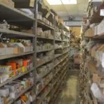 Industrial warehouse aisle with metal shelving units stocked with boxed automotive parts and supplies