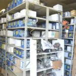 Industrial shelving units stocked with blue and yellow automotive parts boxes and components in warehouse storage area