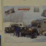 Two people standing between diesel-powered vehicles equipped for expedition, with Power Stroke Diesel and Built Ford Tough logos visible