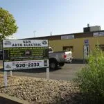 Auto electric repair shop storefront with yellow metal building, service sign, and parked trucks