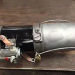 Automotive windshield wiper motor assembly with metal housing, electric motor, and mechanical linkage components on wooden surface.